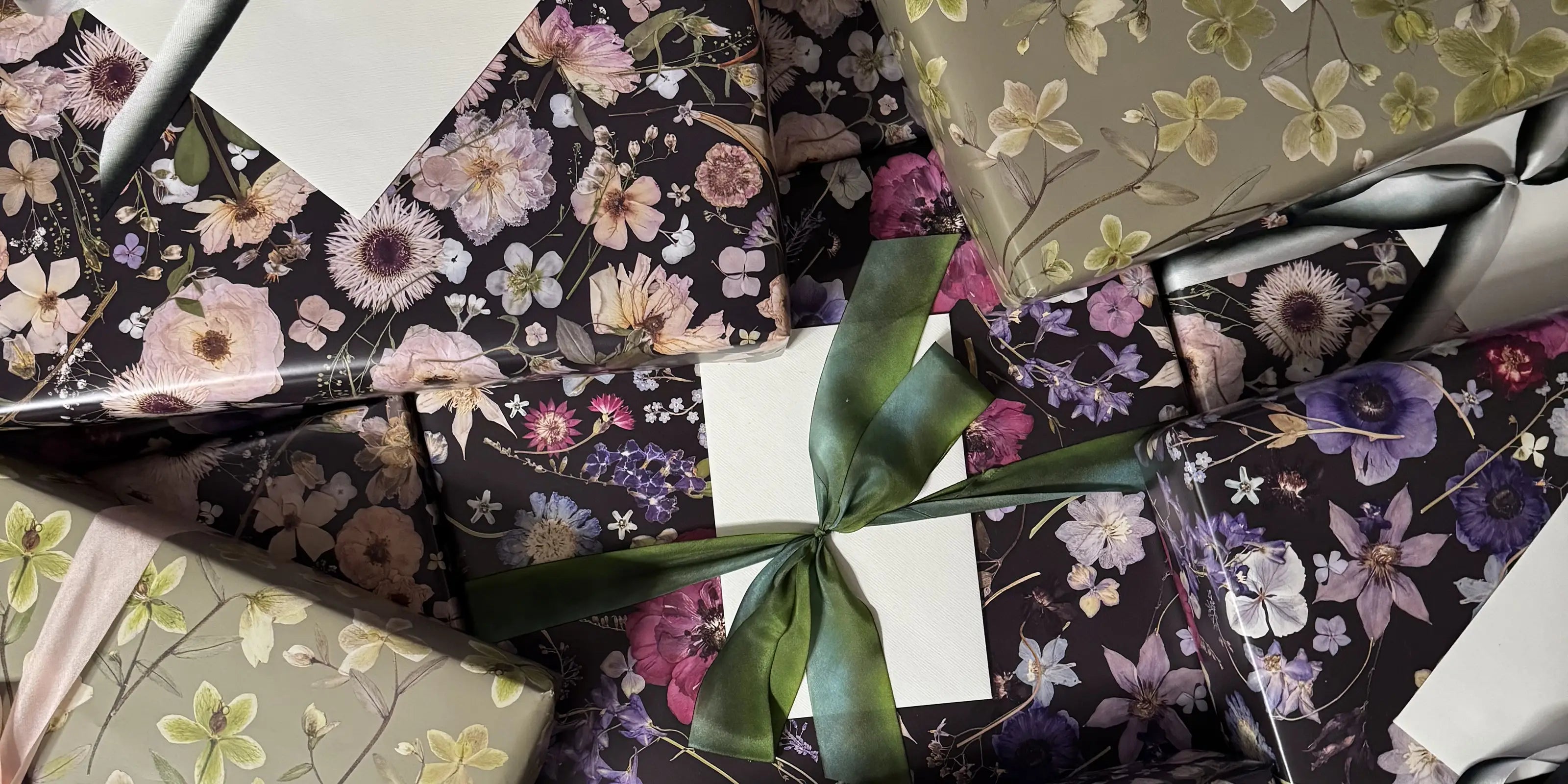 A collection of beautifully wrapped gifts with floral patterns. The boxes feature lush flowers in various colors, accented by green and pink ribbons, creating an elegant and festive atmosphere.