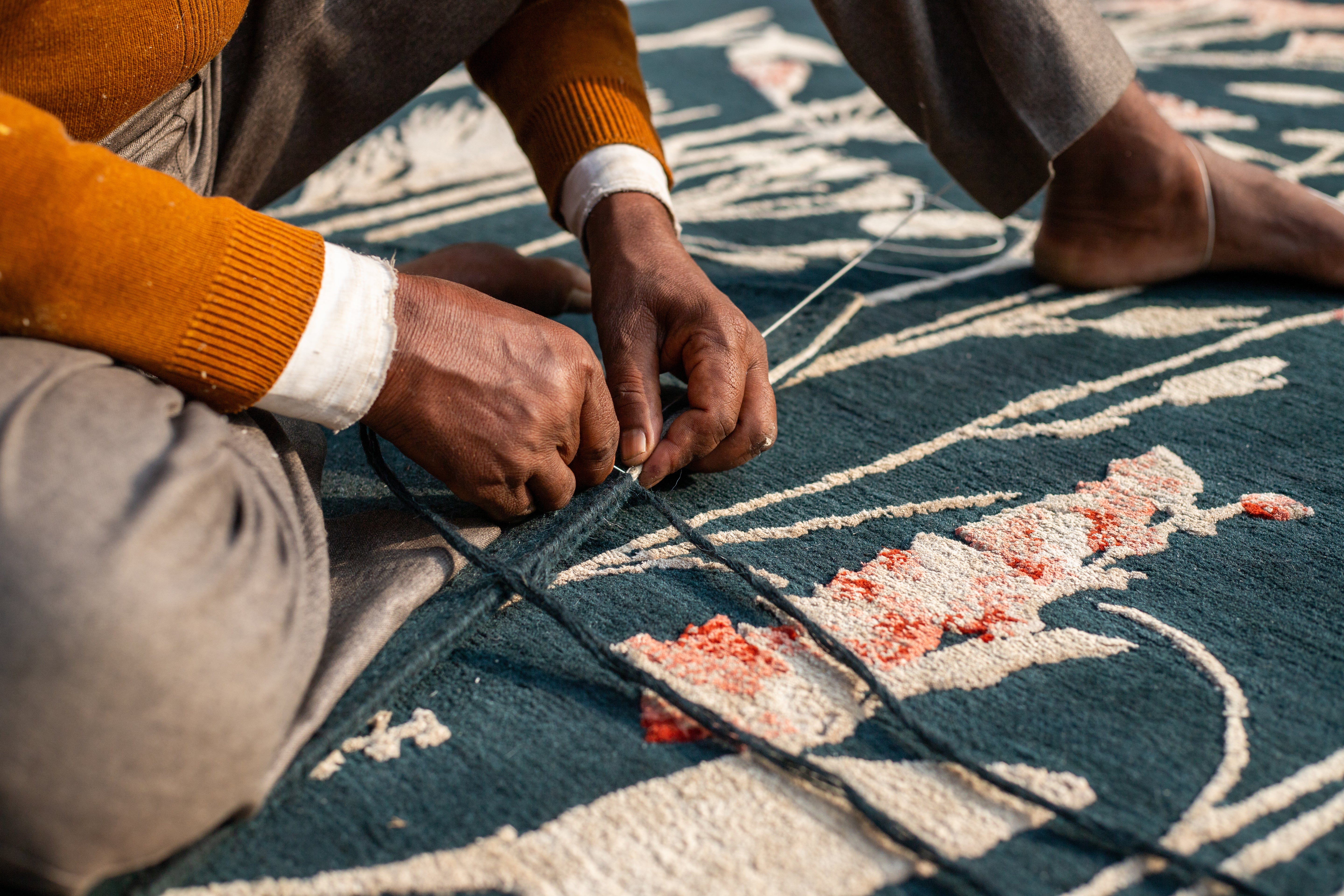 Person working on a rug with intricate floral patterns