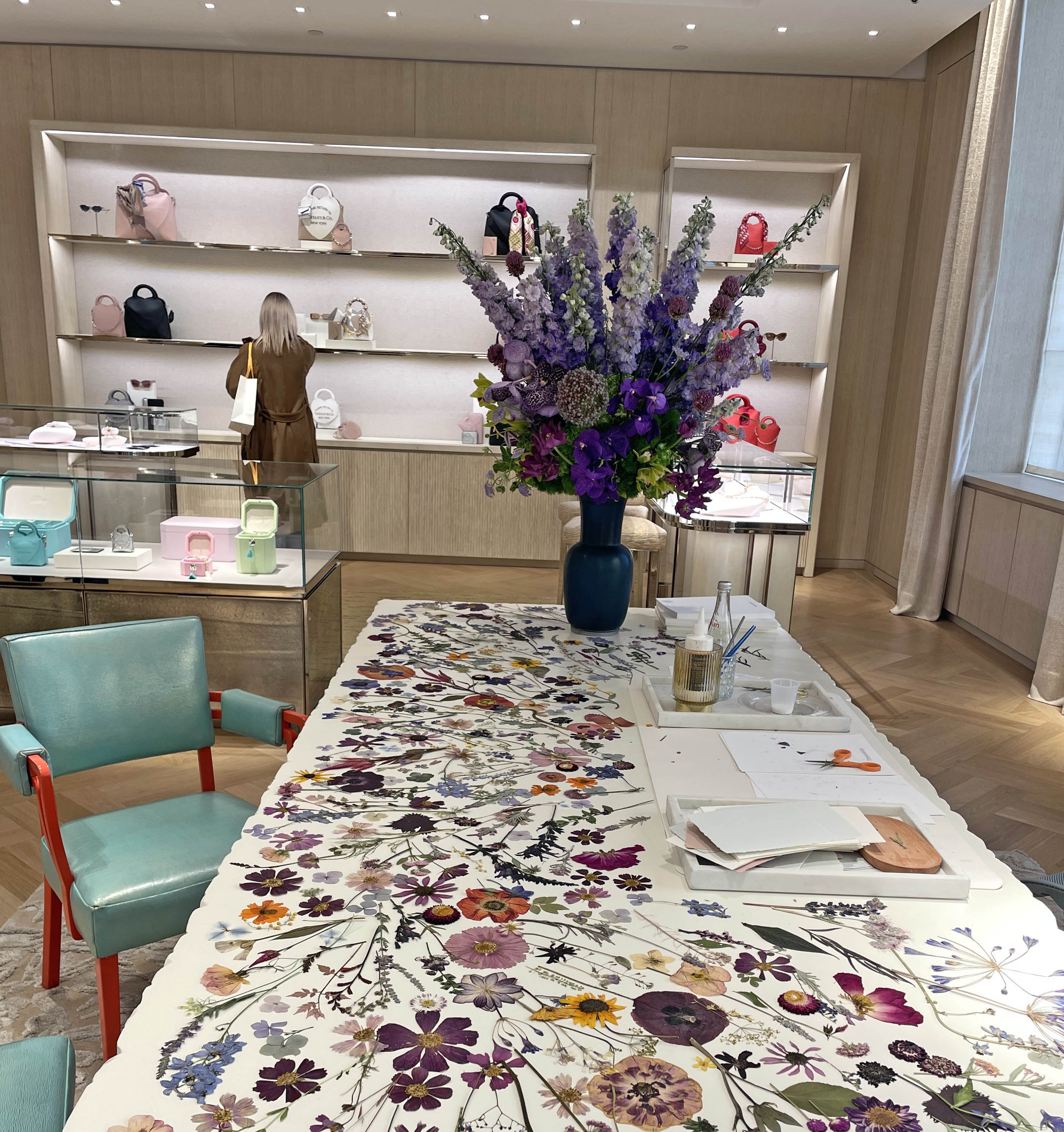 Decorative table with floral tablecloth in a stylish room with shelves and chairs.