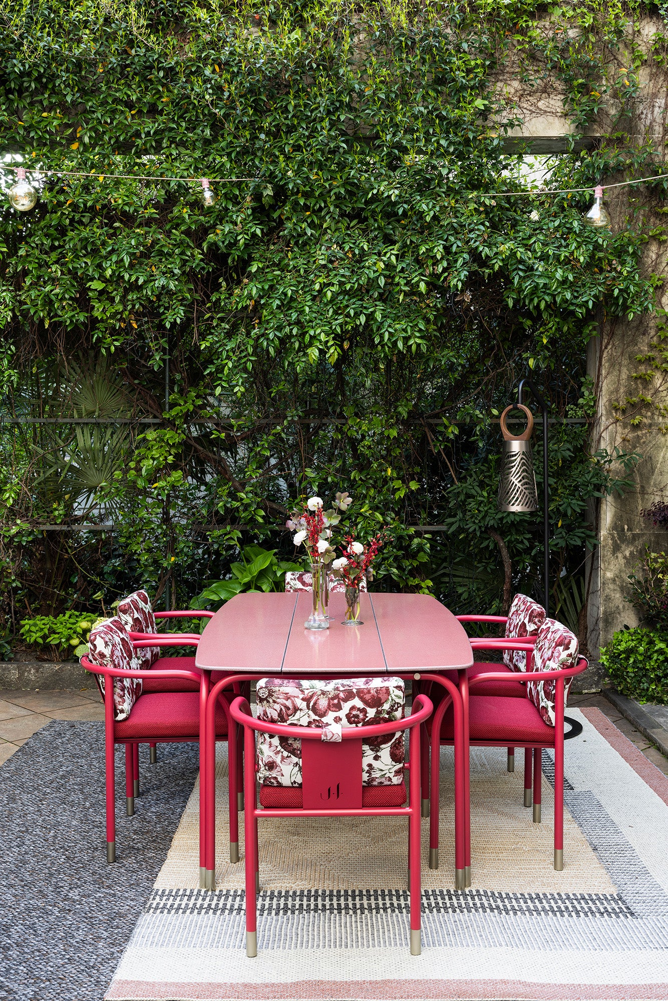 Red outdoor dining set with floral cushions against a green foliage background