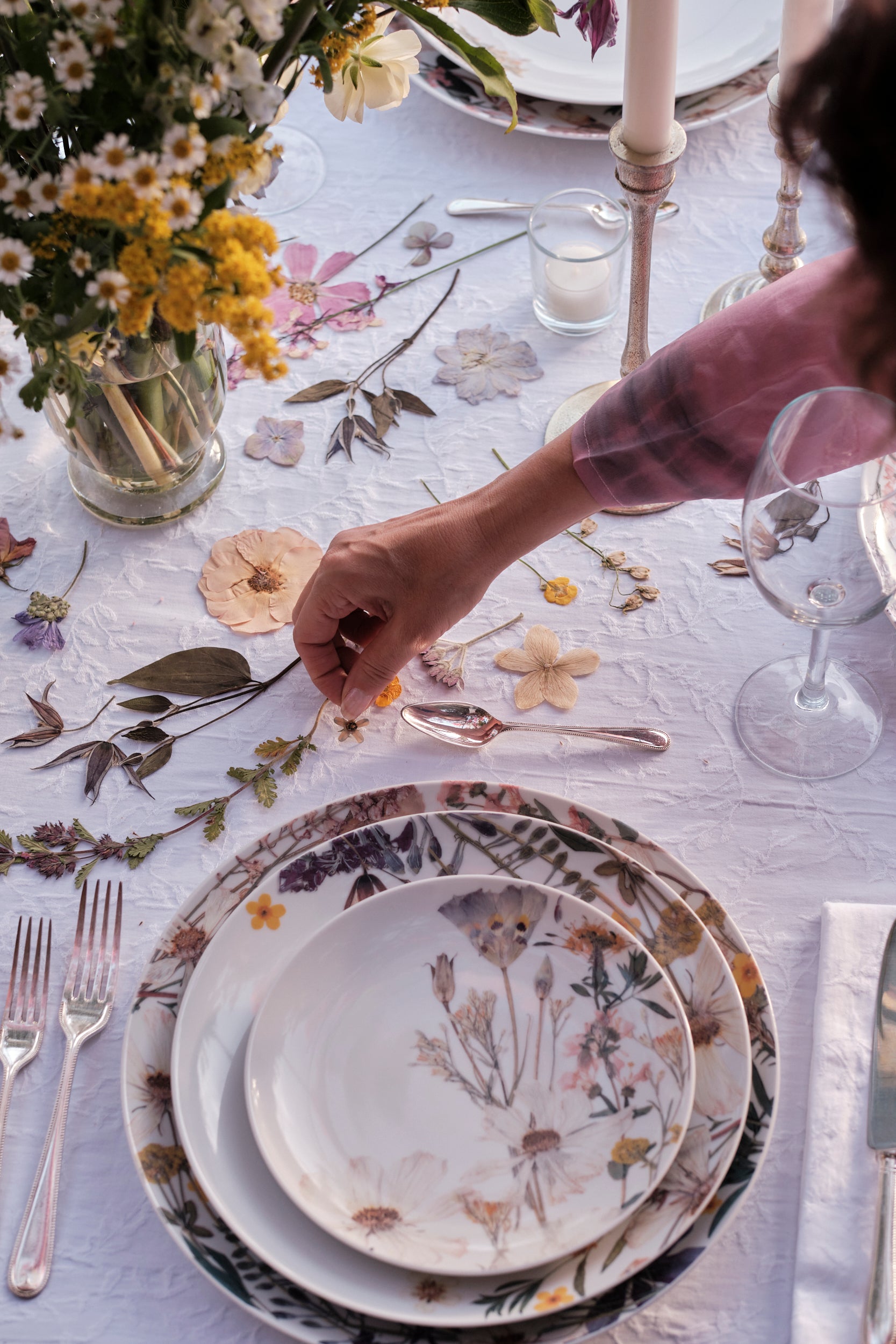 Decorative table setting with floral plates, cutlery, and a vase of flowers.