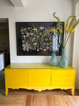 Yellow cabinet with decorative elements and a framed floral print in a room setting