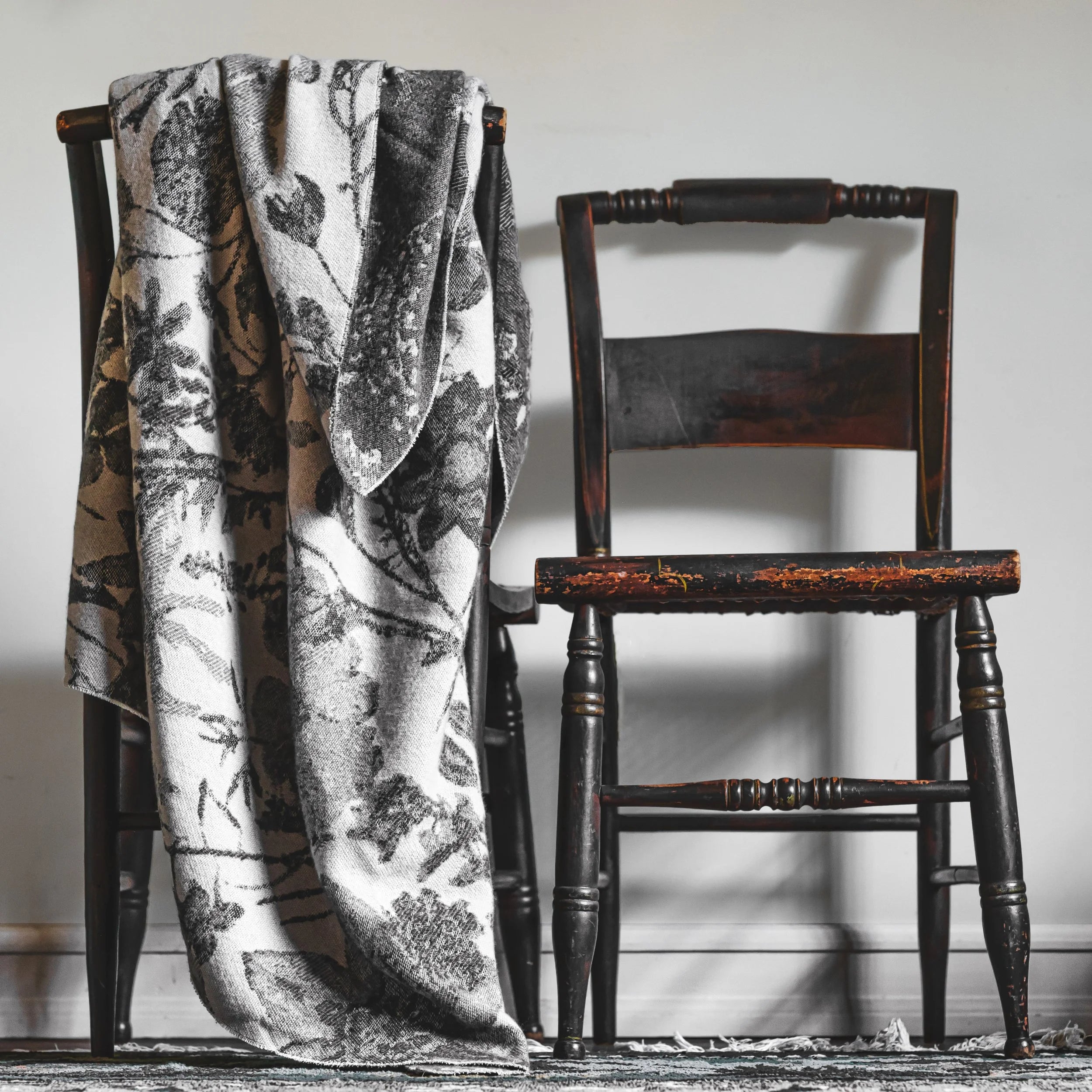 Floral-patterned blanket draped over a wooden chair against a plain wall.