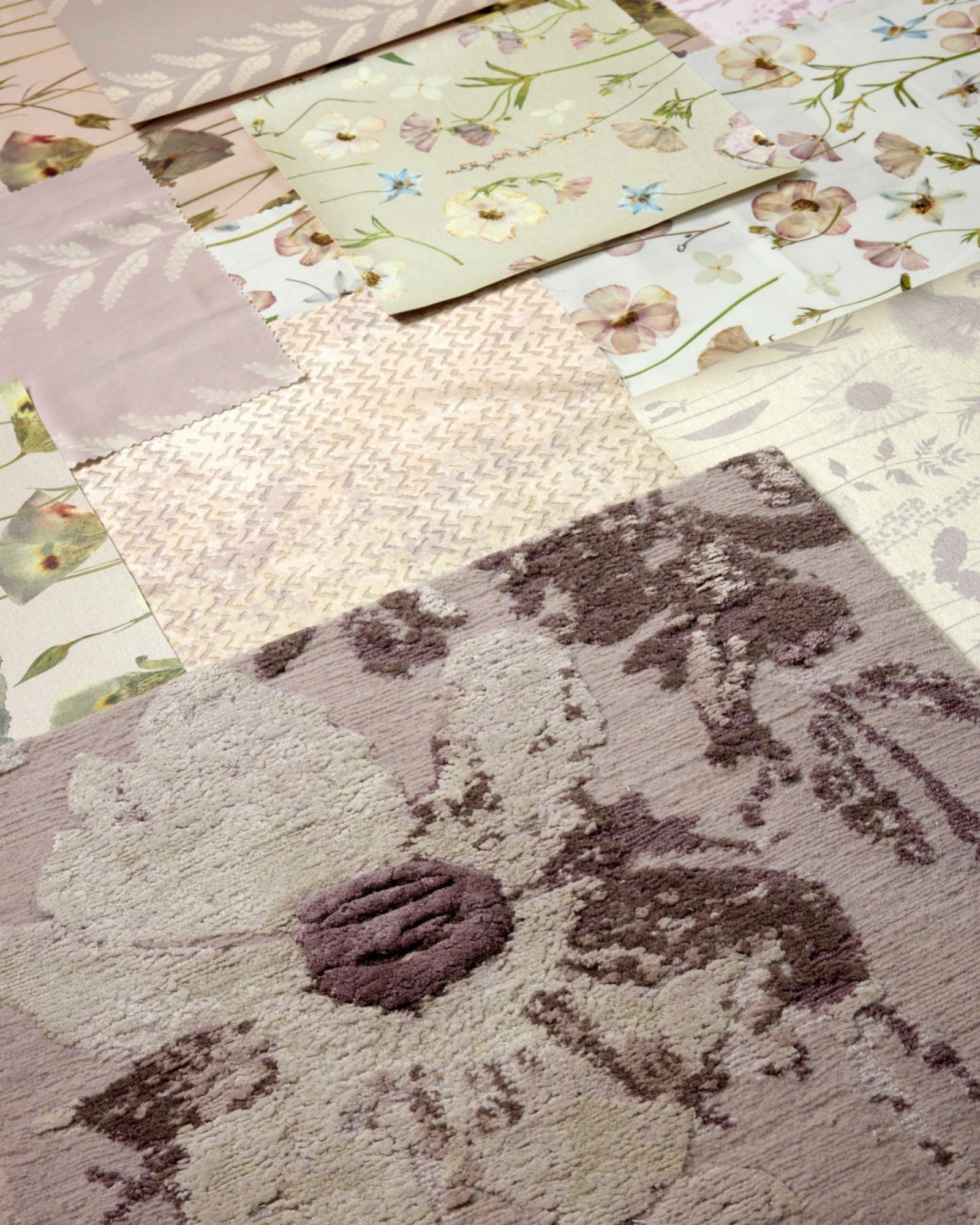 A close-up of a textured floral area rug in muted taupe, beige, and brown tones, laid over a patchwork arrangement of coordinating fabric swatches.